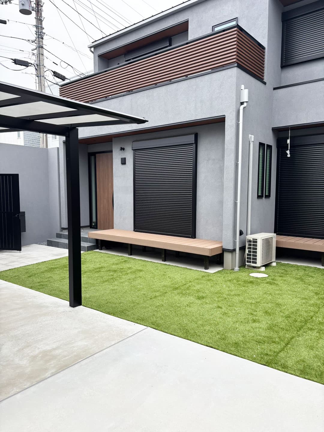 シックでモダンな住宅の前に広がるウッドデッキと芝生の庭